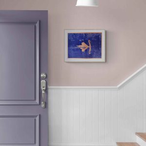 A lavender door with a silver handle is adjacent to a staircase with white paneling. A framed swan artwork in blue and copper hangs on the light pink wall.