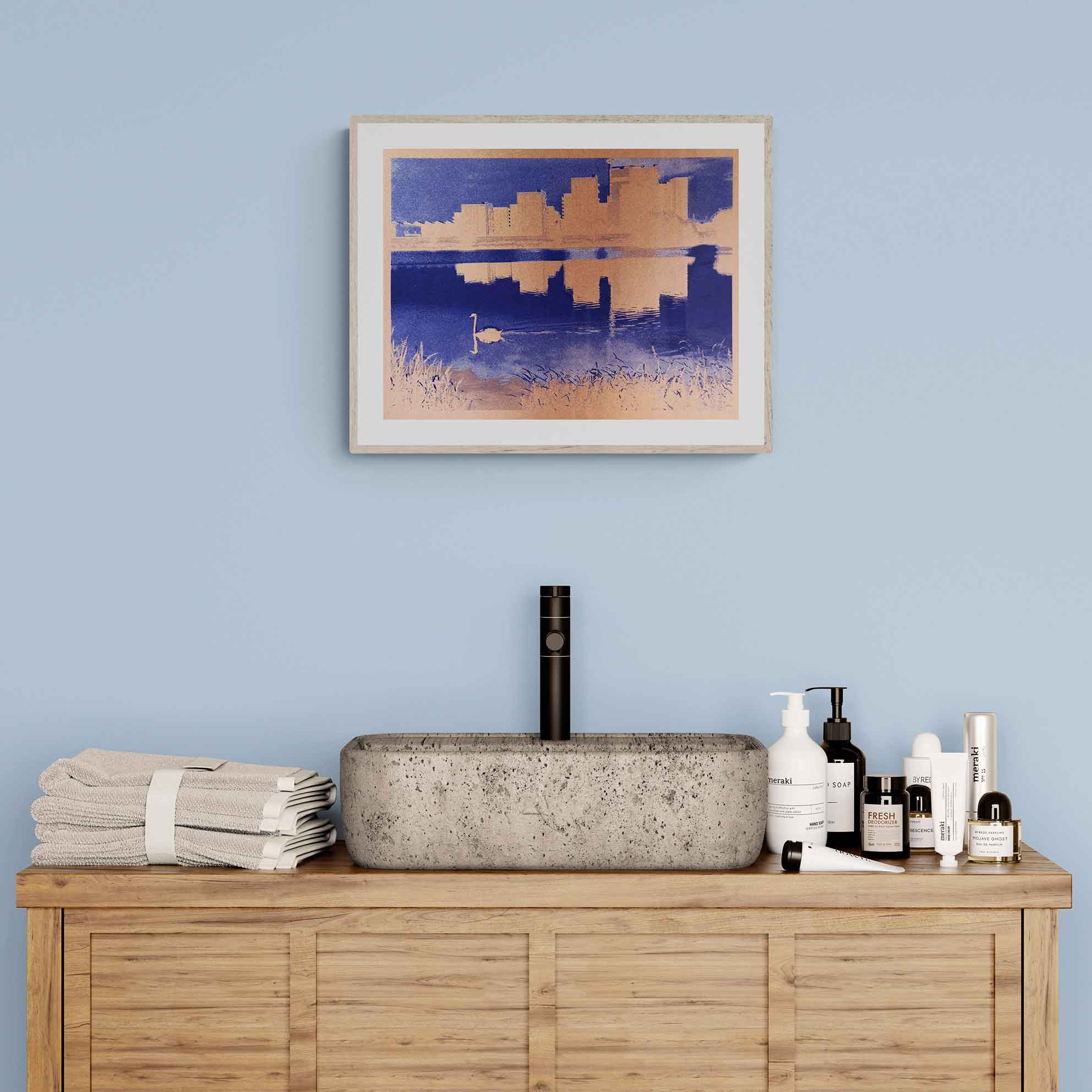 A minimalist bathroom setup with a wooden vanity, a concrete sink, and neatly arranged toiletries. A framed cityscape with a swan in front of it art piece hangs on a light blue wall.